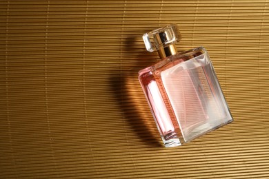 Photo of Luxury women's perfume. Sunlit glass bottle on golden surface, top view. Space for text