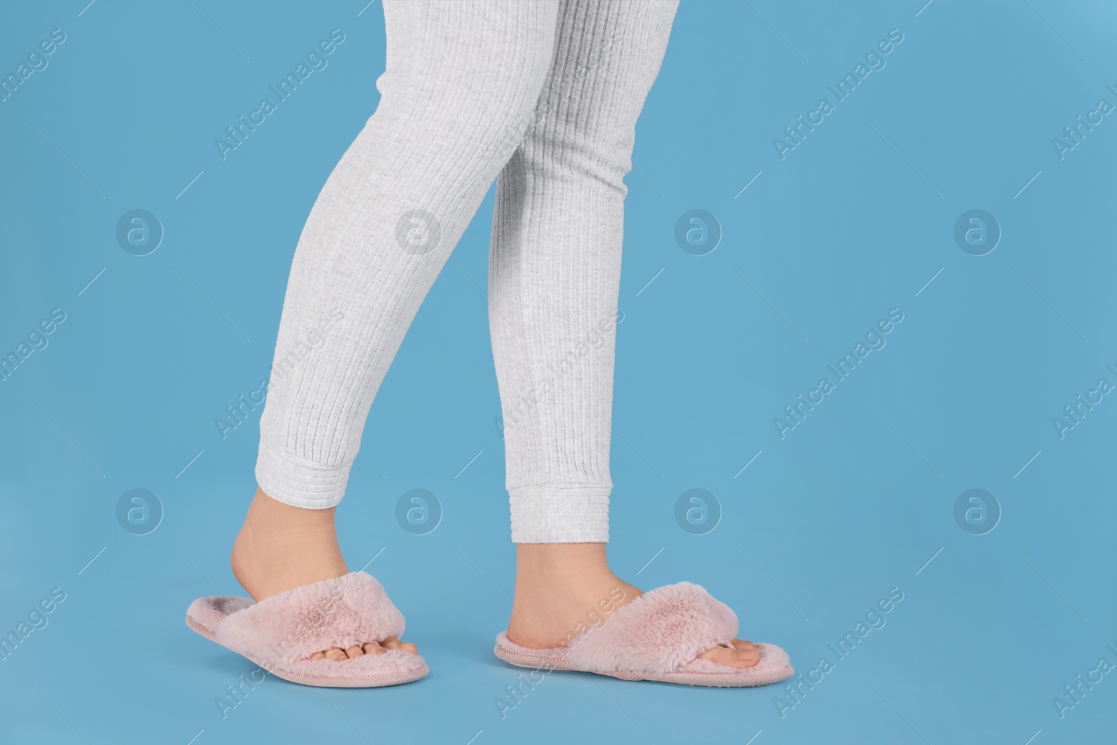 Photo of Woman in fluffy slippers on light blue background, closeup