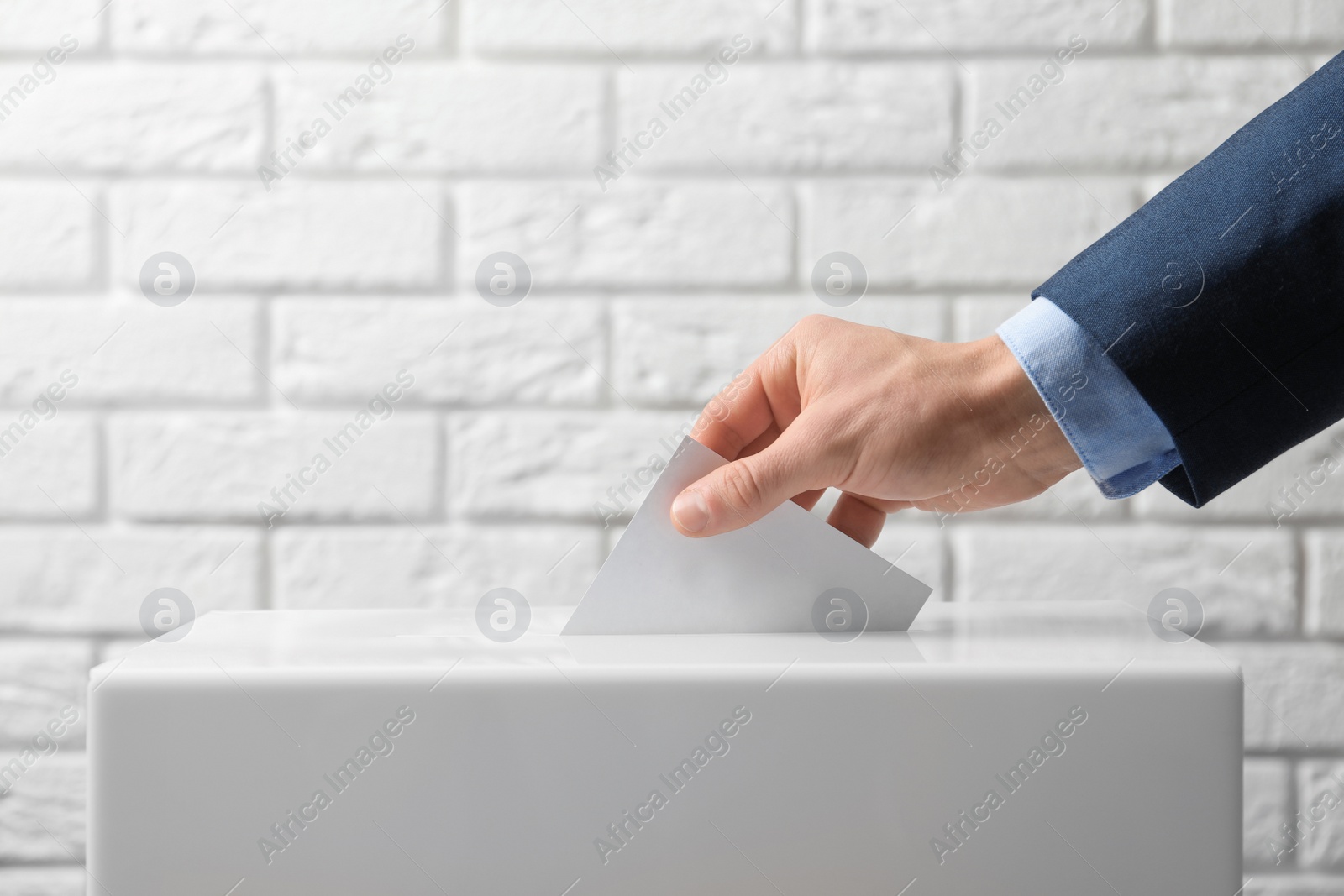 Photo of Man putting his vote into ballot box against brick wall, closeup