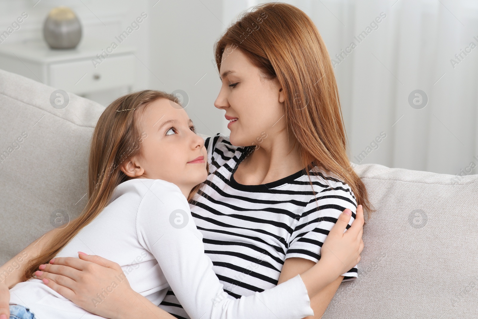 Photo of Mother hugging her cute daughter on sofa at home