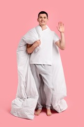 Photo of Happy man in pyjama holding blanket on pink background