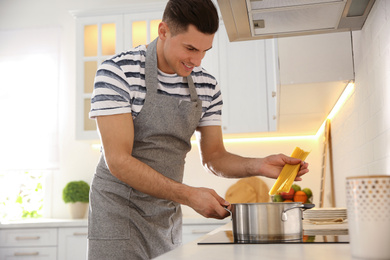 Handsome man cooking pasta on stove in kitchen