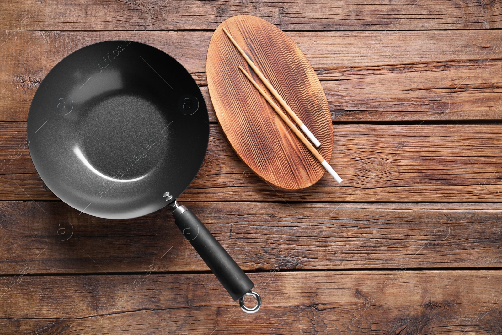 Photo of Empty iron wok and chopsticks on wooden table, flat lay. Space for text
