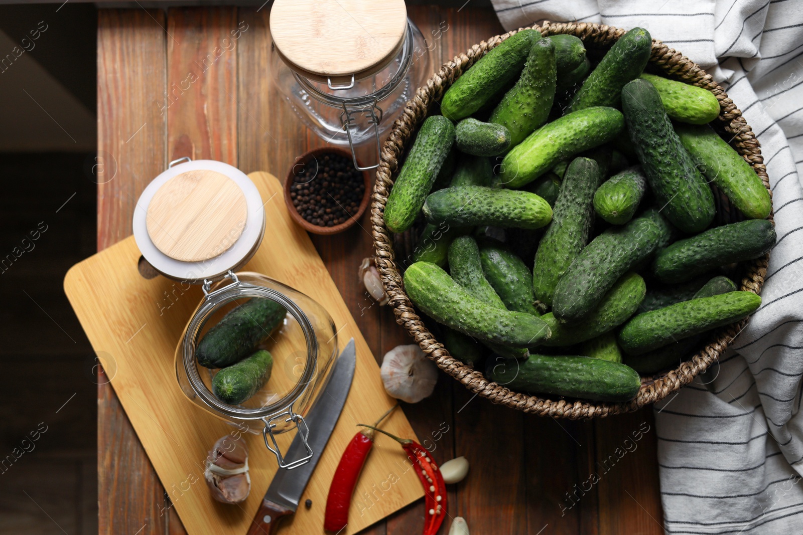 Photo of Fresh cucumbers, other ingredients and jars on wooden table, flat lay. Pickling vegetables