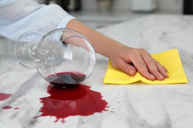Photo of Woman cleaning spilled wine on white marble table indoors, closeup