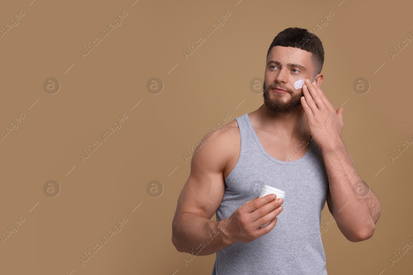 Photo of Handsome man applying cream onto his face on pale brown background, space for text