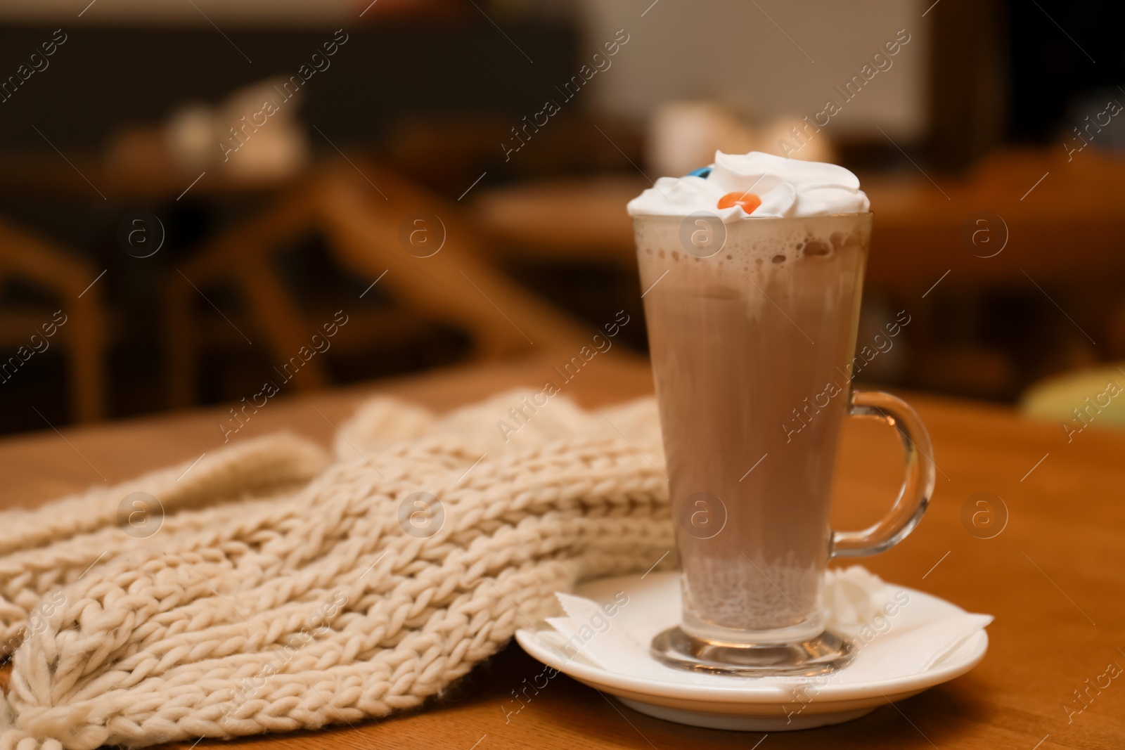 Photo of Cup of aromatic cacao and knitted scarf on table against blurred background