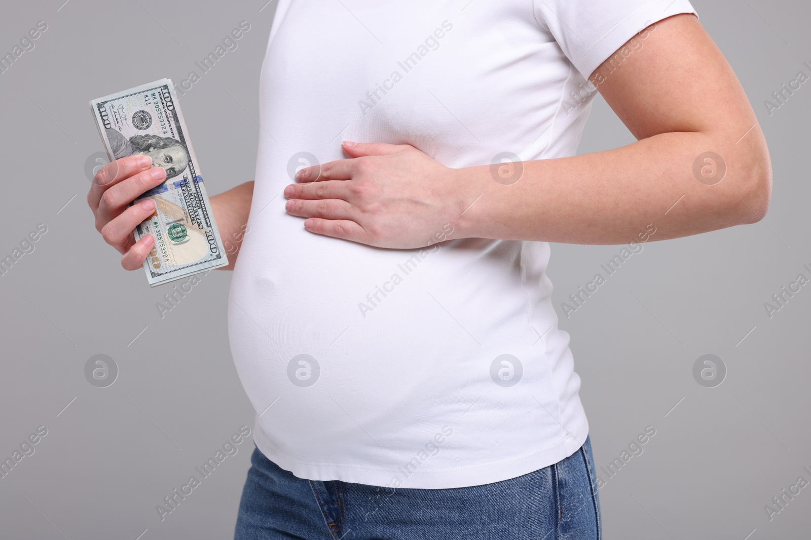 Photo of Surrogate mother. Pregnant woman with dollar banknotes on light grey background, closeup