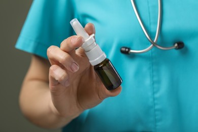 Photo of Woman holding nasal spray bottle on olive background, closeup