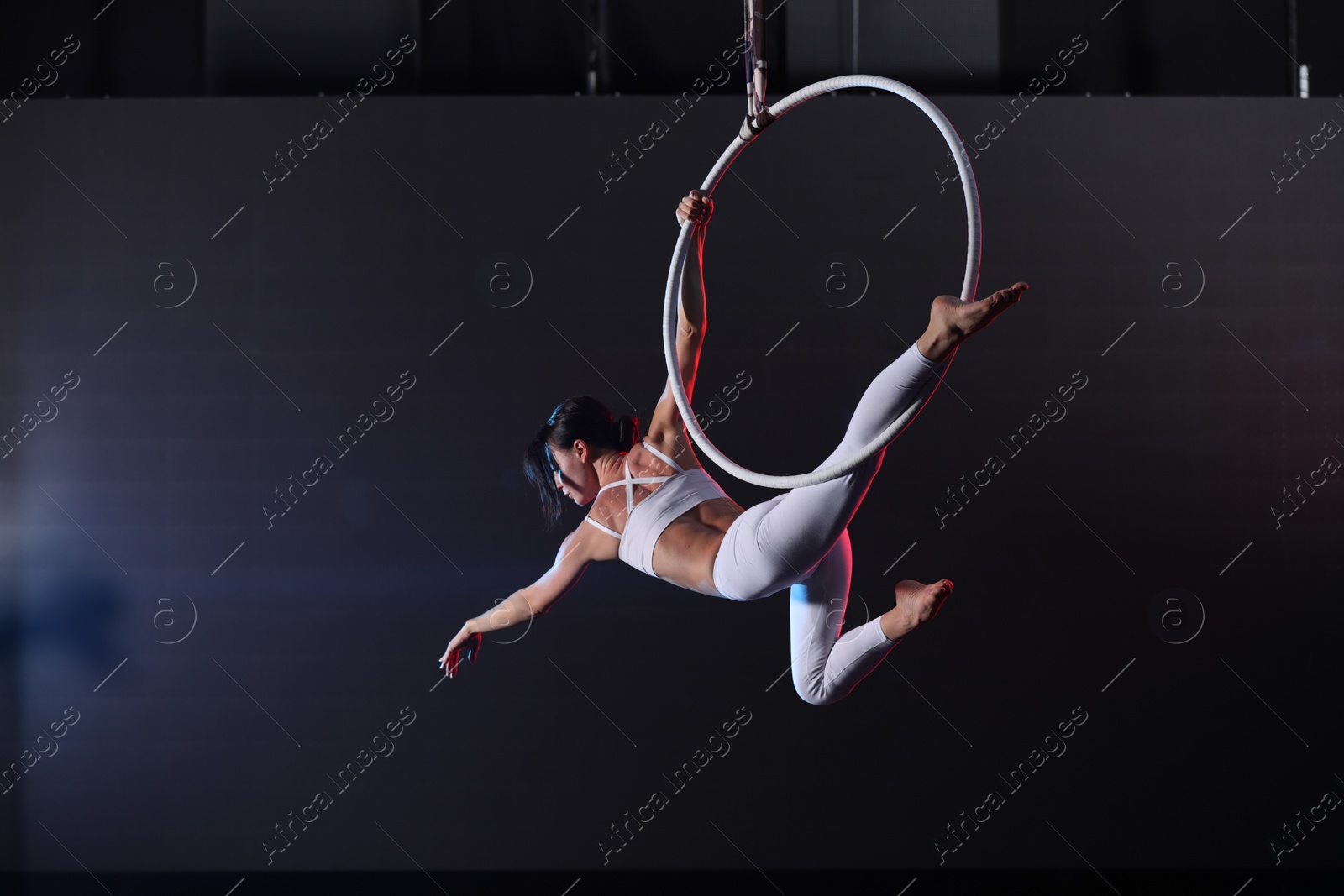 Photo of Young woman performing acrobatic element on aerial ring indoors