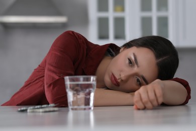 Photo of Depressed woman at white marble table with antidepressant pills and glass of water indoors