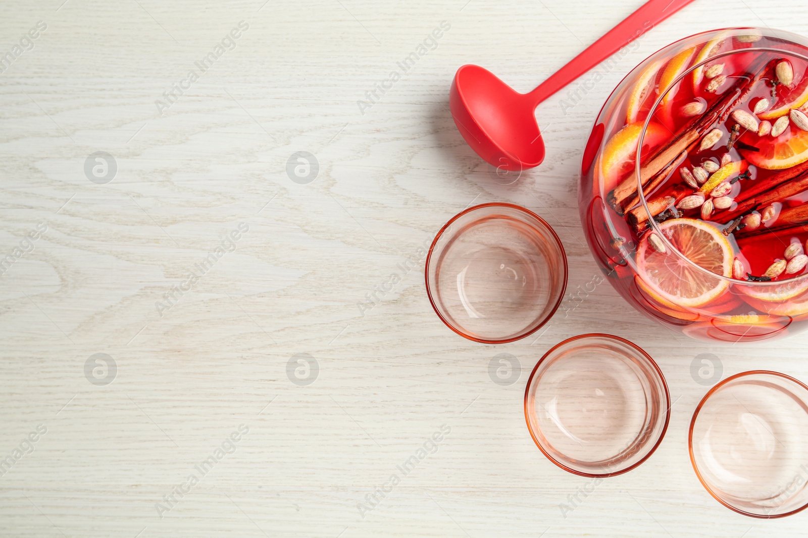 Photo of Bowl of delicious aromatic punch drink, ladle and empty glasses on white wooden table, flat lay. Space for text