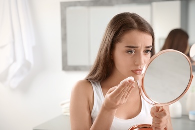 Young woman with beautiful eyelashes removing makeup indoors