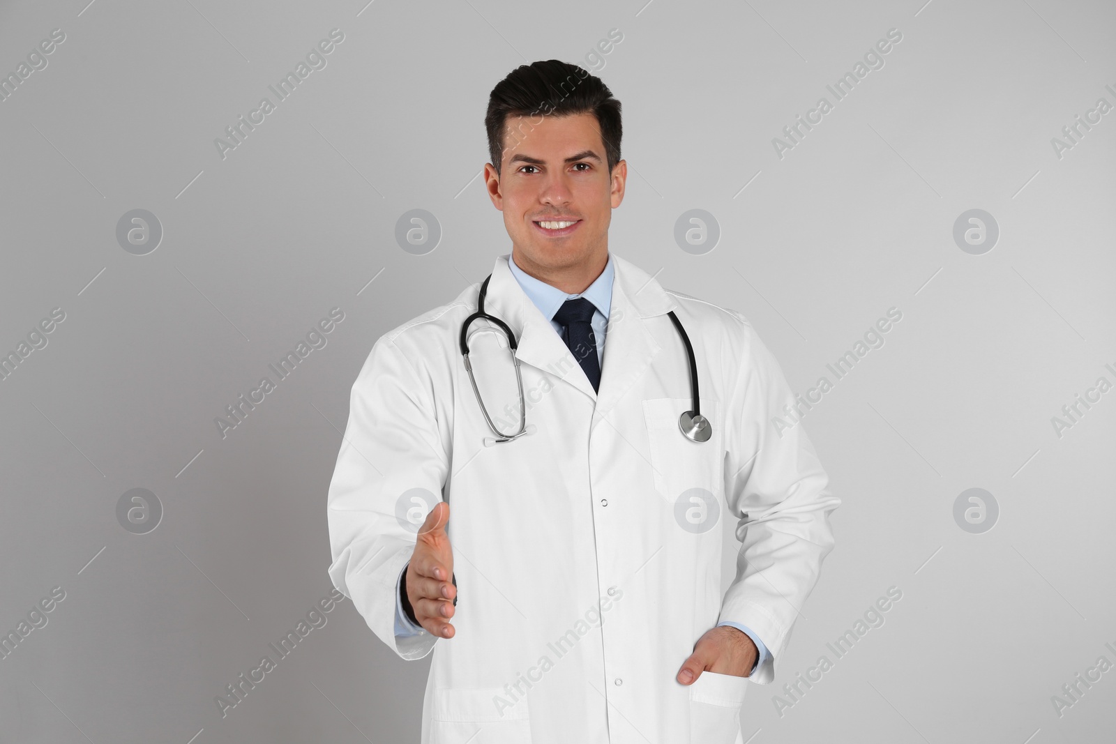 Photo of Happy male doctor offering handshake on light grey background