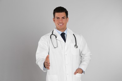 Photo of Happy male doctor offering handshake on light grey background