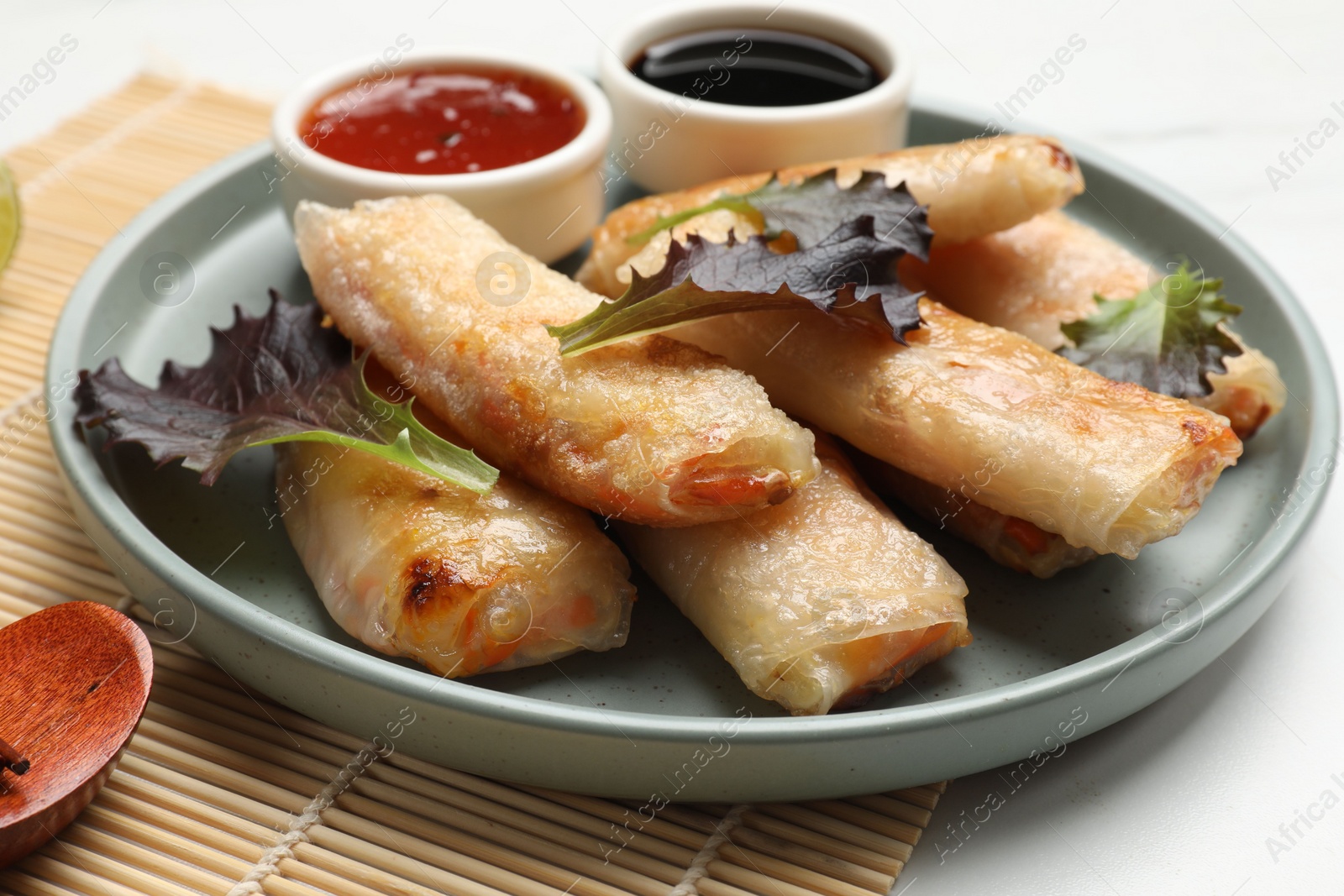 Photo of Tasty fried spring rolls, lettuce and sauces on white marble table, closeup