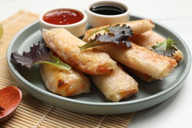 Photo of Tasty fried spring rolls, lettuce and sauces on white marble table, closeup