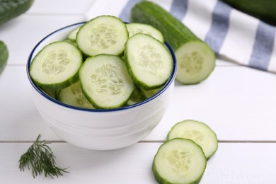 Photo of Cut cucumber in bowl, fresh vegetable and dill on white wooden table, closeup