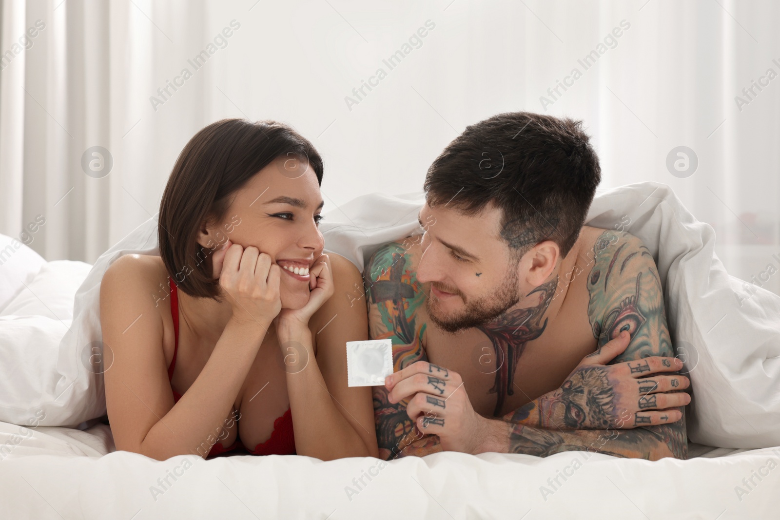 Photo of Young couple holding condom in bedroom. Safe sex