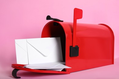 Open red letter box with envelopes on pink background, closeup