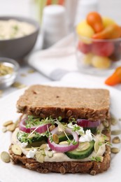 Tasty vegan sandwich with cucumber, onion, hummus and pumpkin seeds on plate, closeup