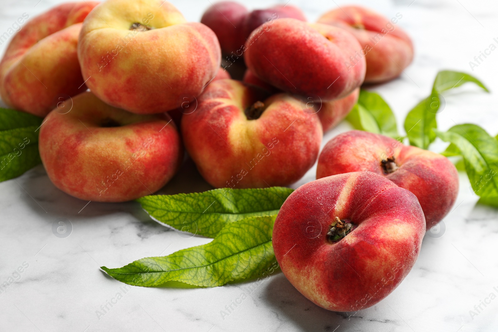 Photo of Fresh ripe donut peaches with leaves on white marble table, closeup