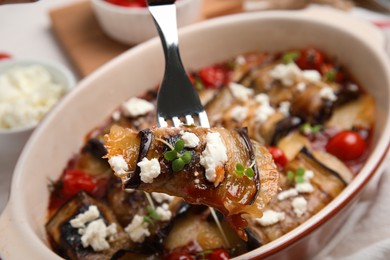 Fork with tasty eggplant roll over baking dish, closeup