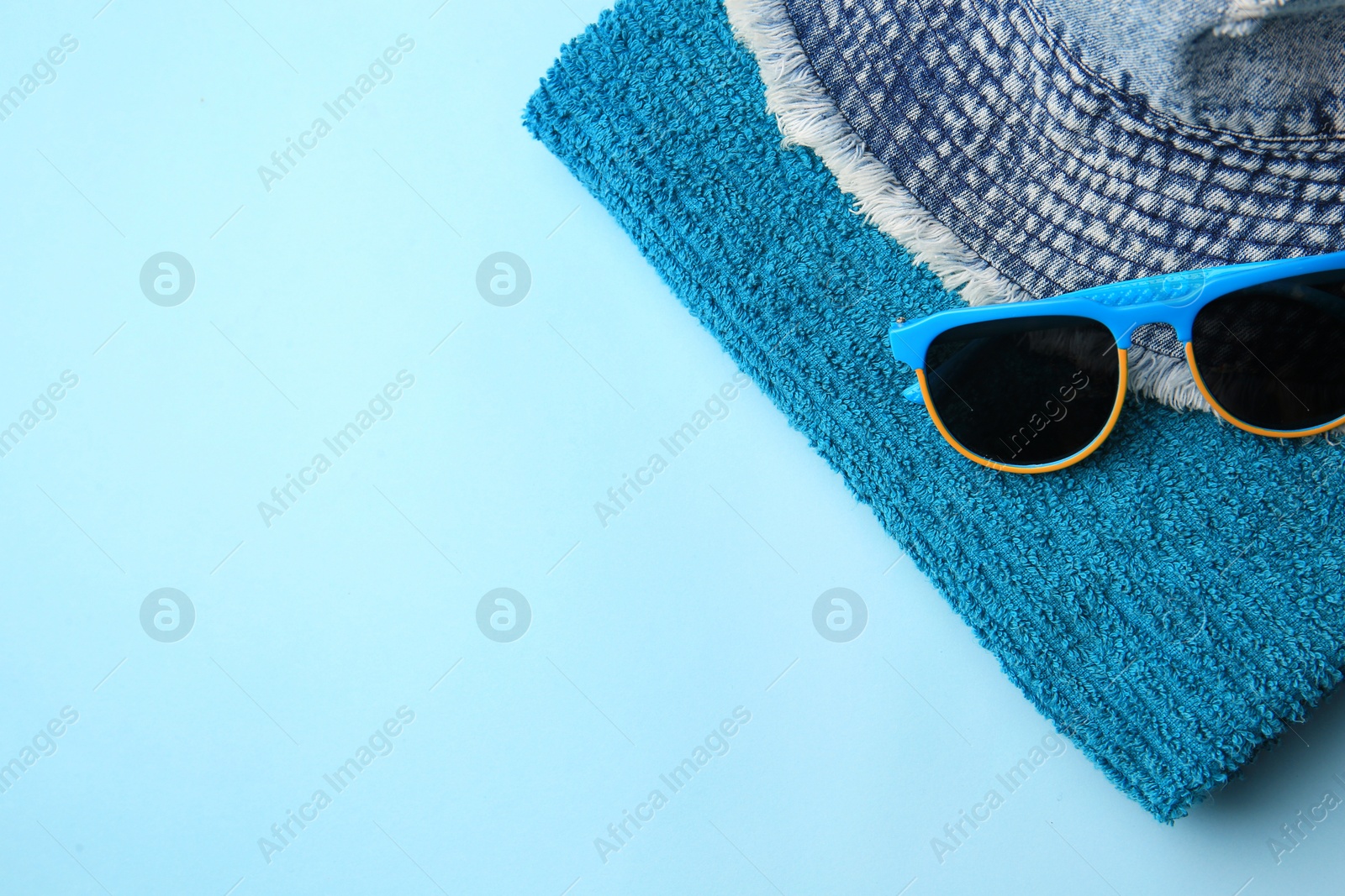 Photo of Towel, denim hat and sunglasses on light blue background, flat lay with space for text. Beach accessories