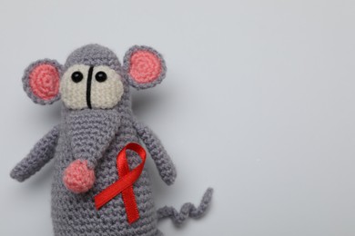 Photo of Cute knitted toy mouse with red ribbon on light grey background, top view and space for text. AIDS disease awareness
