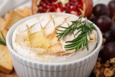 Photo of Tasty baked camembert and rosemary in bowl on blurred background, closeup