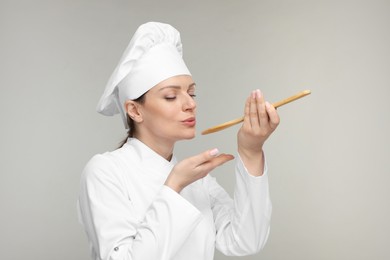 Photo of Woman chef in uniform tasting something on grey background