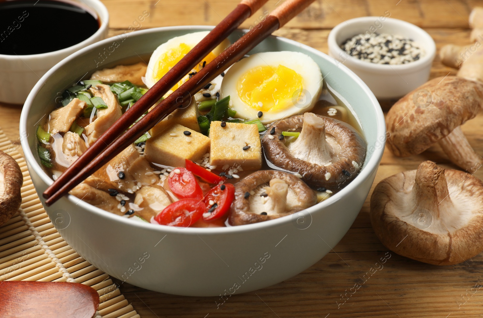 Photo of Bowl of delicious ramen and ingredients on wooden table, closeup. Noodle soup