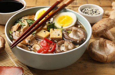 Bowl of delicious ramen and ingredients on wooden table, closeup. Noodle soup