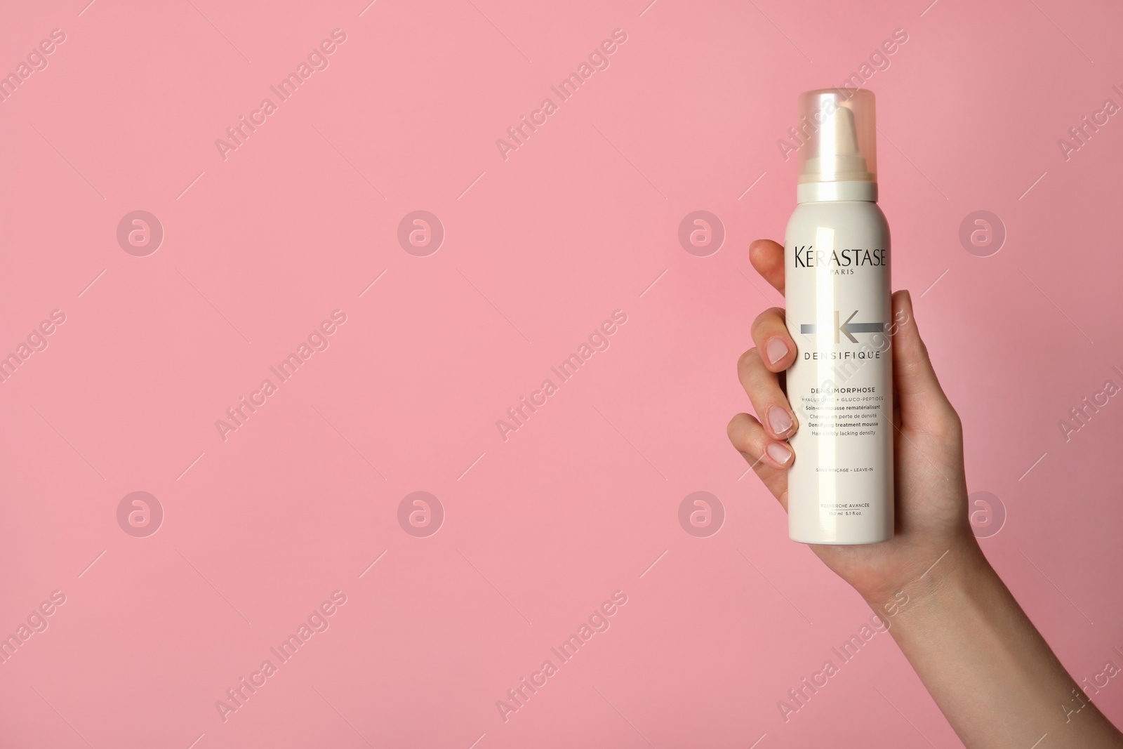 Photo of MYKOLAIV, UKRAINE - SEPTEMBER 09, 2021: Woman holding bottle of Kerastase hair care cosmetic product on pink background, closeup. Space for text