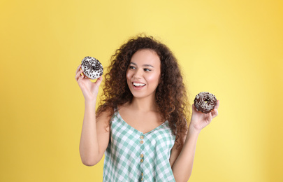 Beautiful African-American woman with donuts on yellow background