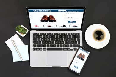 Photo of Online store website on laptop screen. Computer, smartphone, stationery, coffee and houseplant on black background, flat lay