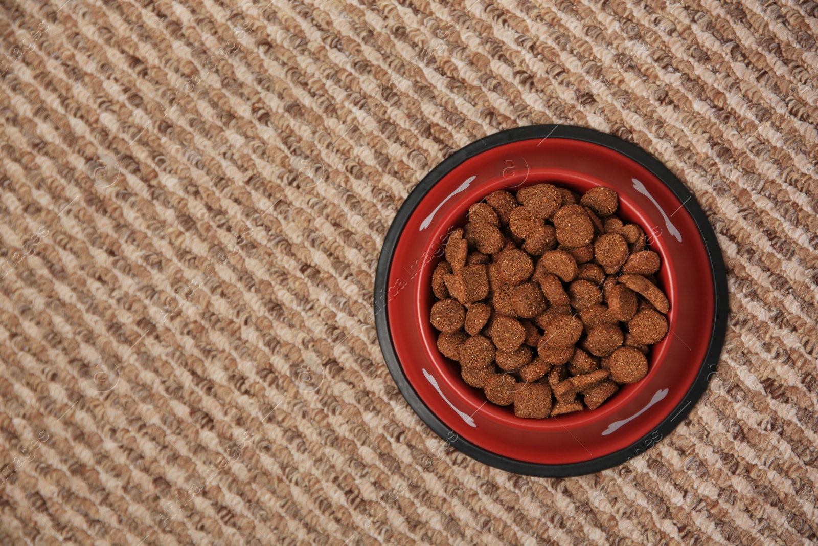 Photo of Dry dog food in feeding bowl on soft carpet, top view. Space for text