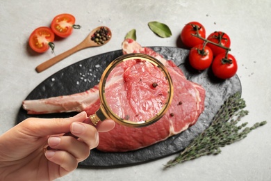 Image of Woman with magnifying glass focusing on fresh raw meat, closeup. Food control 