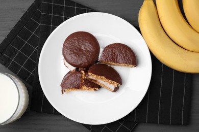 Photo of Tasty sweet choco pies, bananas and glass of milk on grey wooden table, flat lay
