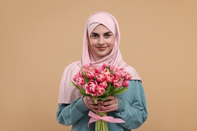 Happy woman in hijab with beautiful bouquet on beige background