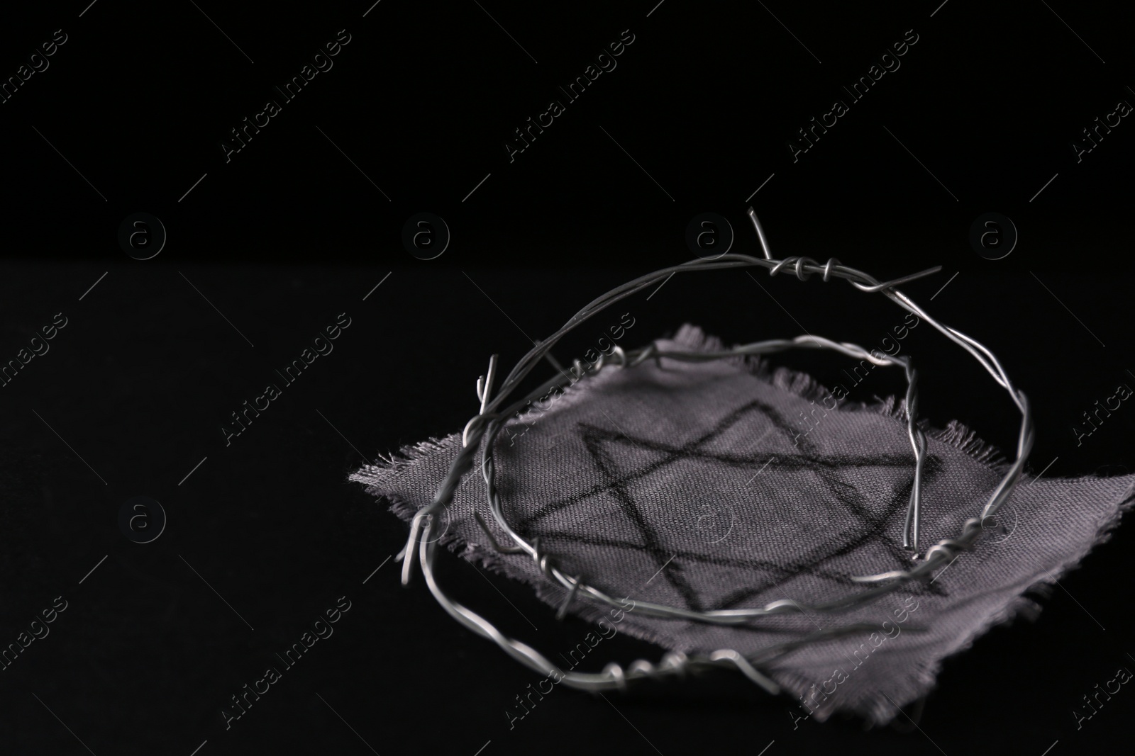 Photo of Fabric with star of David and barbed wire on black background, space for text. Holocaust memory day