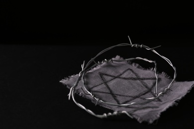 Photo of Fabric with star of David and barbed wire on black background, space for text. Holocaust memory day