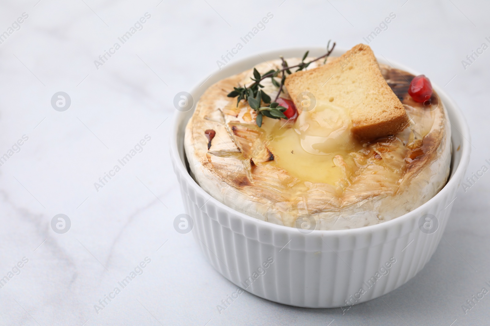 Photo of Tasty baked camembert with crouton and thyme on white marble table, closeup. Space for text