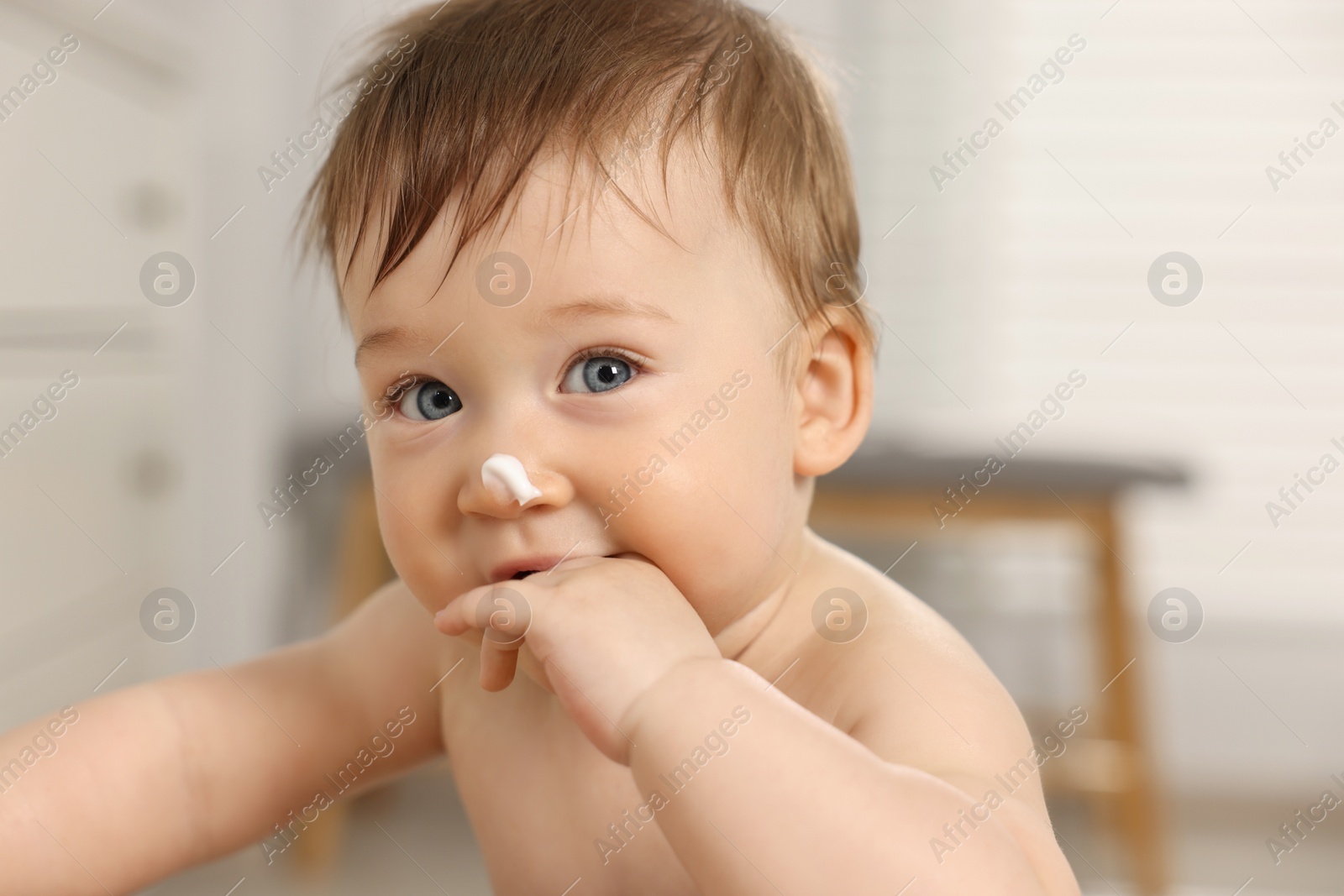 Photo of Cute little baby with moisturizing cream on face indoors