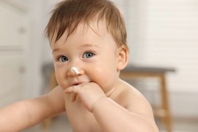 Cute little baby with moisturizing cream on face indoors