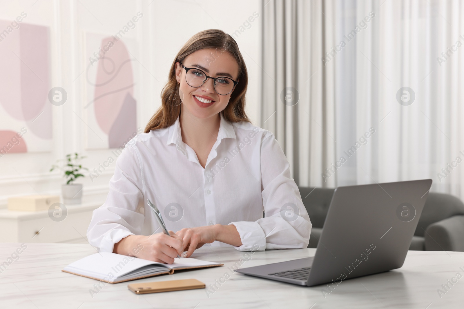 Photo of Happy woman with notebook and laptop at white table in room