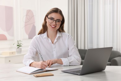 Happy woman with notebook and laptop at white table in room