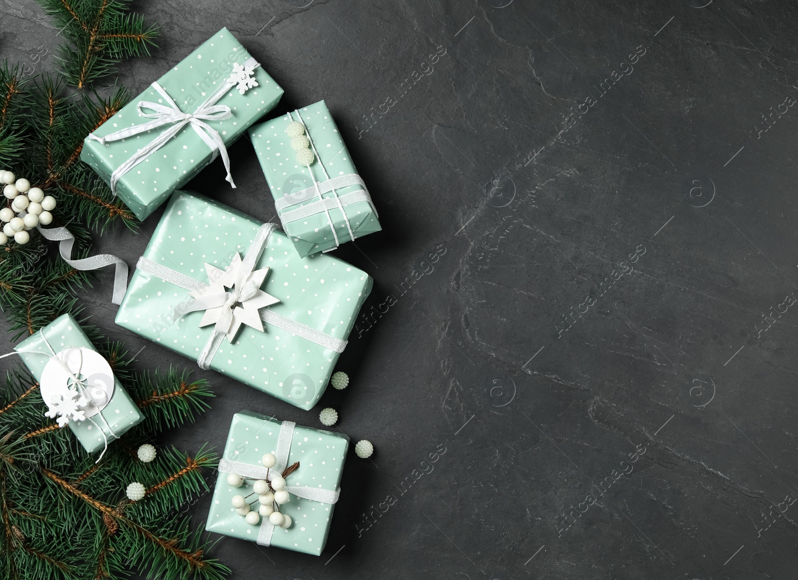 Photo of Christmas gift boxes with fir branches on dark grey background, flat lay. Space for text