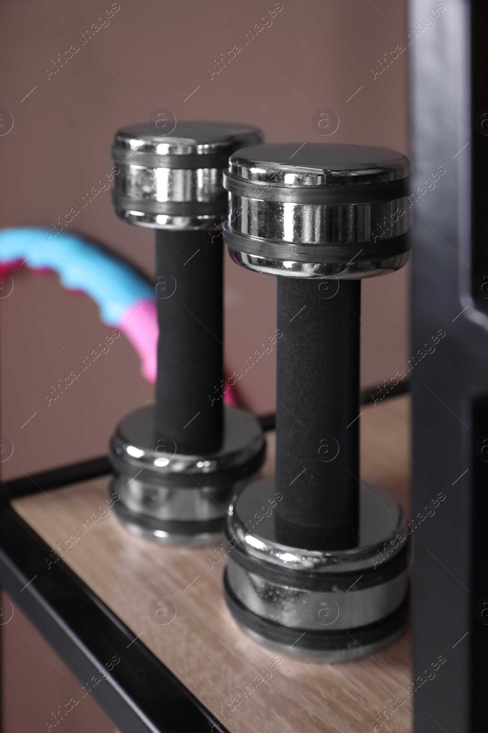 Photo of Metal dumbbells on shelf indoors, closeup. Sports equipment