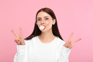 Photo of Beautiful woman in glasses blowing bubble gum and gesturing on pink background
